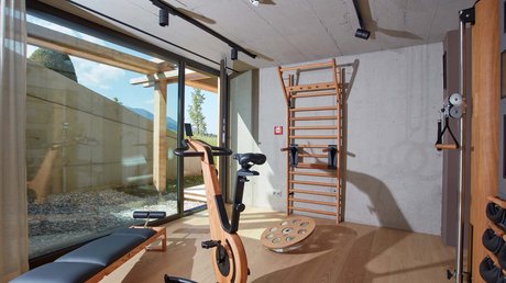 Aussicht auf Traumurlaub in Bad Tölz Moderne Fitnessgeräte aus Holz in einem hellen Fitnessraum mit Fenster zur Terrasse