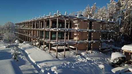 Aussicht auf Traumurlaub in Bad Tölz Modernes Holzgebäude im Schnee umgeben von verschneiten Bäumen und blauem Himmel