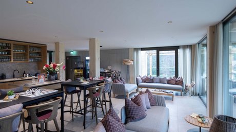 Aussicht auf Traumurlaub in Bad Tölz Moderne Lounge mit Sofas, Tischen, Stühlen und großen Fenstern